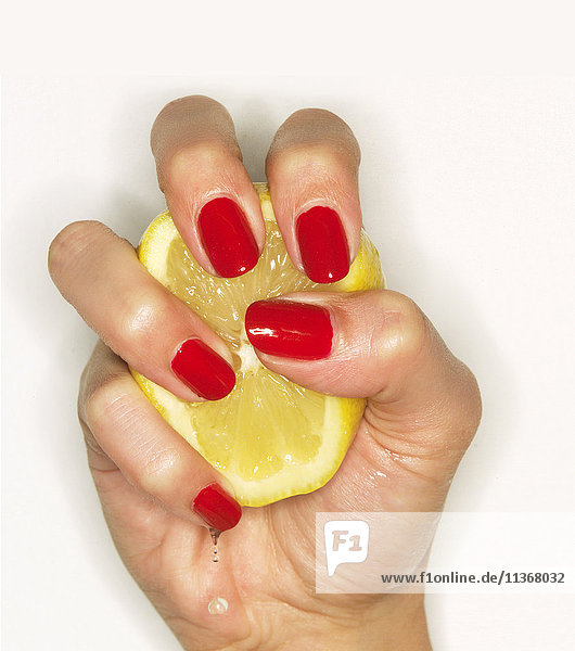 Hand of woman with red nail polish squeezing lemon