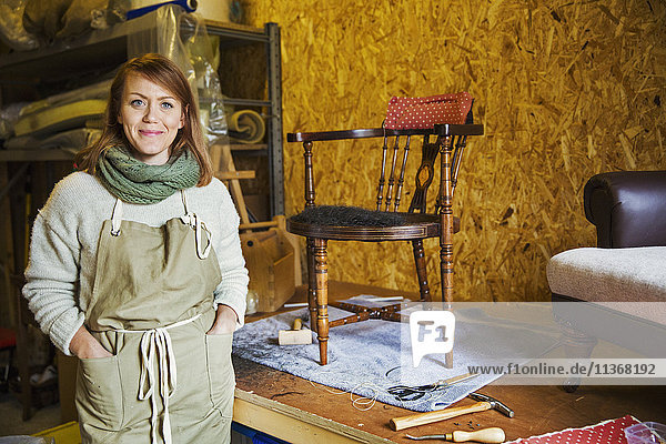 Upholstery workshop. A young woman with hands in her apron pockets. Work in progress.