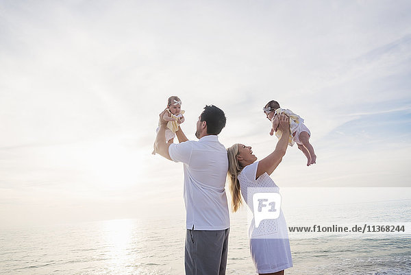 Happy family with two baby girls (2-5 months) at beach in sunlight