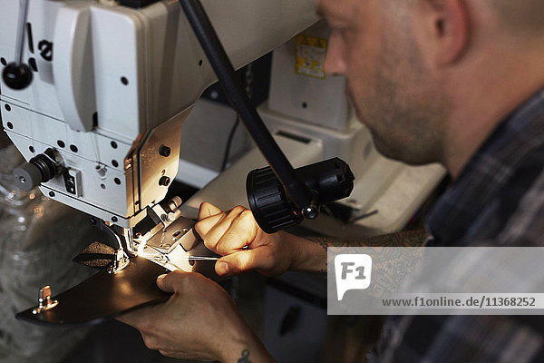 Ein Mann  der eine Industrienähmaschine benutzt und handgefertigte Lederwaren näht.