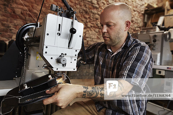 Ein Lederarbeiter  Handwerker  der mit einer Industrienähmaschine auf Ledermaterial näht und eine Tasche herstellt.