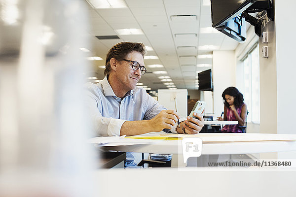 Ein Mann sitzt an einem Tisch in einem Büro und schaut auf ein Handy.