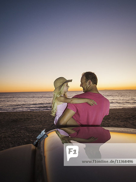 Vater trägt Tochter (4-5) neben dem Auto am Strand