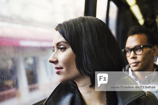 Eine Frau  die in öffentlichen Verkehrsmitteln sitzt und aus dem Fenster schaut  mit einem jungen Mann im Hintergrund.