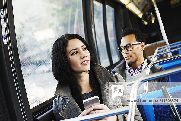 A young man and a young woman sitting on public transport holding their cellphones and looking around.