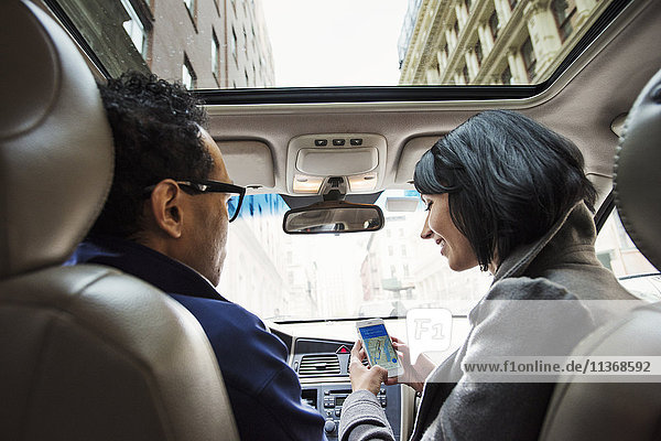 Eine junge Frau und ein junger Mann in einem Auto  die vom Rücksitz aus eine Karte auf dem Display eines Mobiltelefons betrachten.