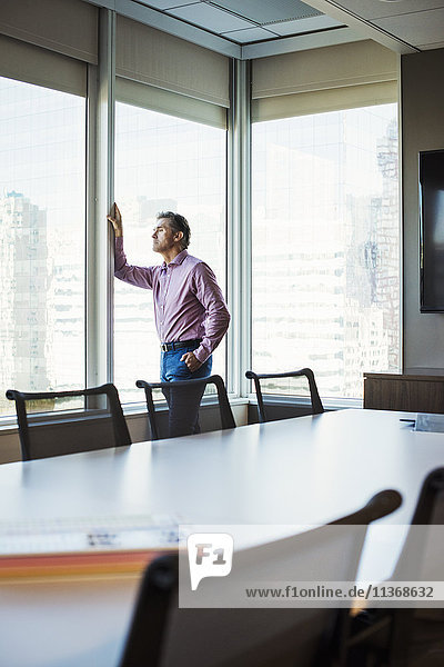 A man in a meeting room looking out of a window at an urban landscape.