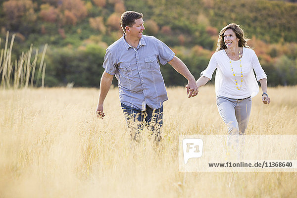 Smiling couple holding hands while walking in field