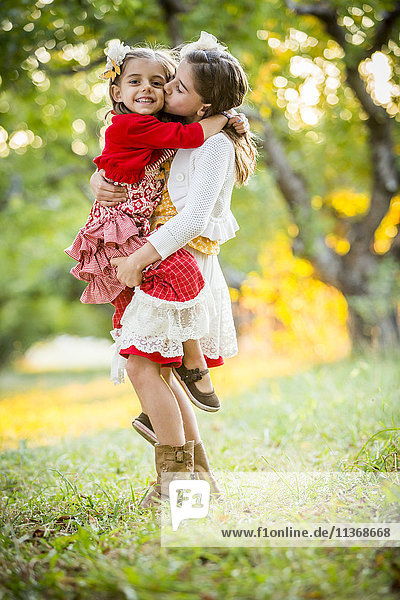 Girl holding and kissing sister in cherry orchard