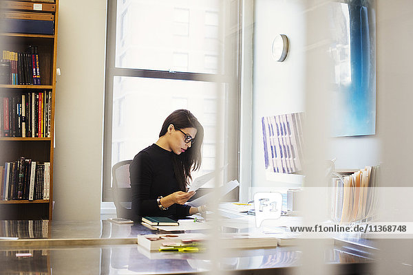 Eine junge Frau sitzt an einem Schreibtisch in einem Büro und sieht sich Papierkram an.