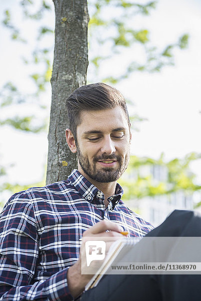 Young man sitting in a park and writing in notepad