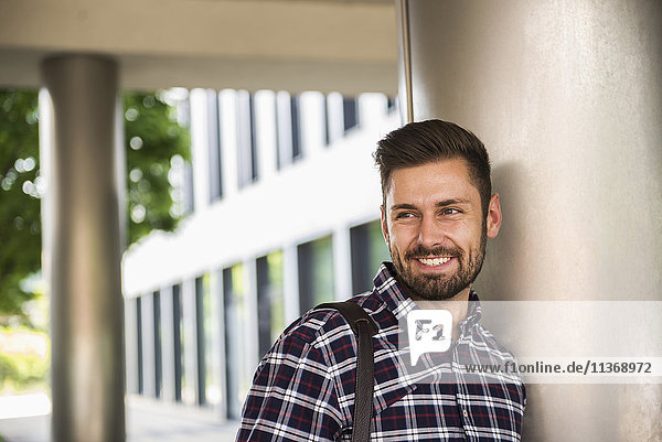 Portrait of a young man smiling and leaning against wall