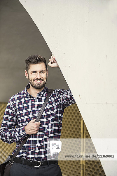 Young man leaning against round arch and smiling