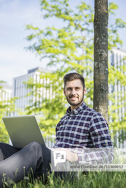 Young man working on laptop and sitting in park