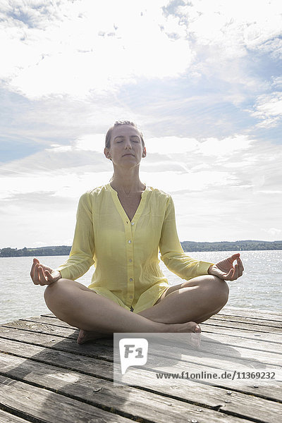 Woman doing lotus pose yoga on jetty at the lake  Ammersee  Upper Bavaria  Germany
