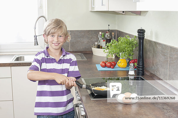 Porträt eines Jungen  der in der Küche Spiegeleier zubereitet
