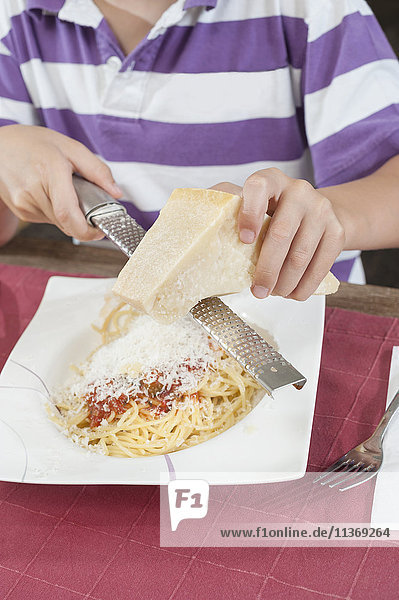 Midsection of a boy grating cheese over pasta