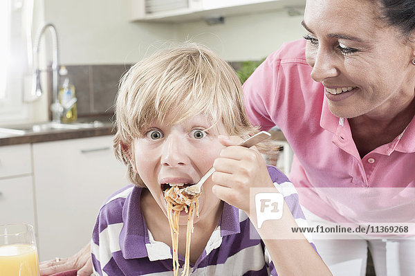 Portrait of a boy eating spaghetti with his mother