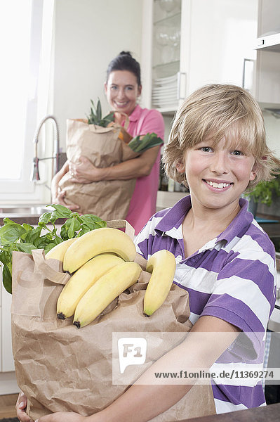 Boy with his mother holding bags of groceries in kitchen