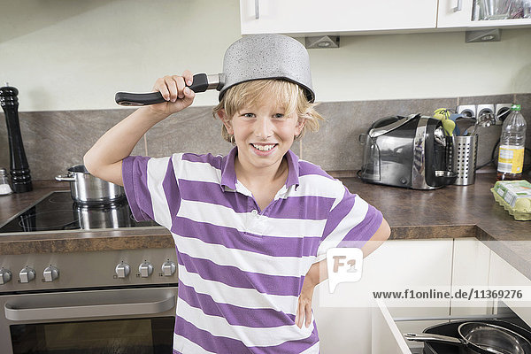 Happy boy with pan on his head in kitchen