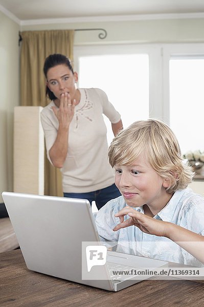 Shocked woman watching her son using laptop in living room
