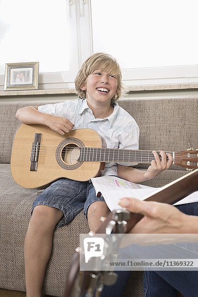 Frau mit ihrem Sohn spielt Gitarre im Wohnzimmer