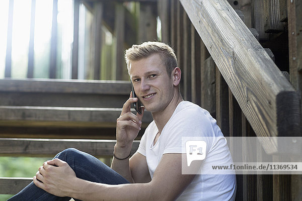 Junger Mann spricht auf einer Treppe mit seinem Handy
