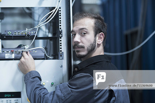 Junger männlicher Ingenieur,  der in einem Technikraum den Stecker eines Routers anschließt