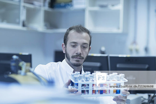 Junger männlicher Wissenschaftler  der ein Reagenzglas in einem Labor untersucht