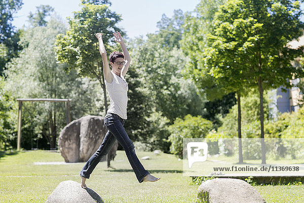 Mature woman jumping from one rock to another rock in the park