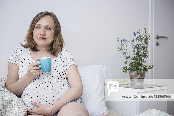 Schwangere Frau trinkt eine Tasse Kaffee im Bett