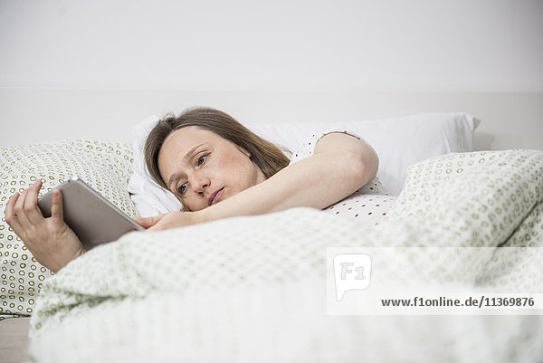 Schwangere Frau im Bett liegend und mit digitalem Tablet