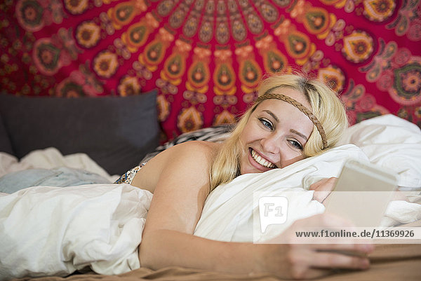 Schöne junge Frau mit Smartphone im Schlafzimmer