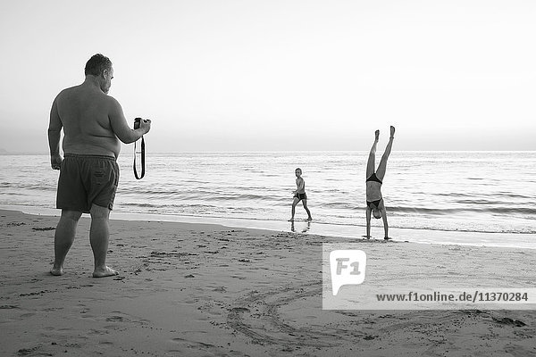 Father taking picture of children on beach