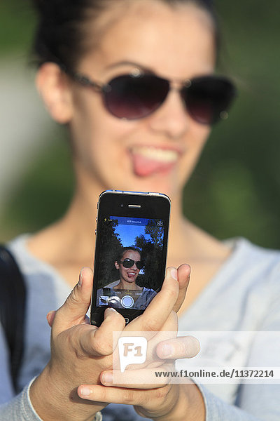 Junge Frau  die einen Selfie mit ihrem Smartphone nimmt.