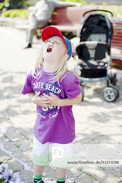Small girl in baseball cap standing in park