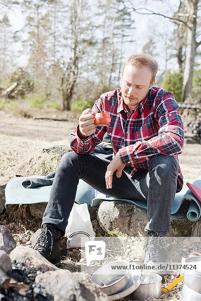 Mann sitzt auf Matte und trinkt im sonnigen Herbstwald
