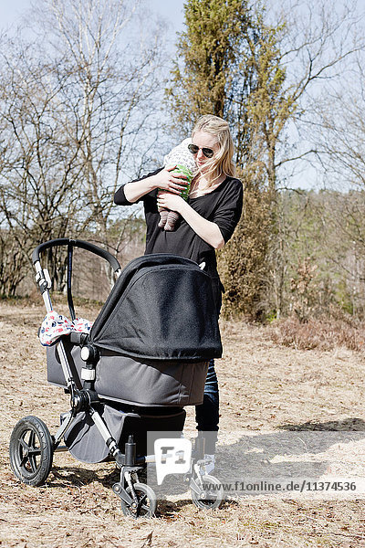 Mother holding baby  standing beside baby carriage