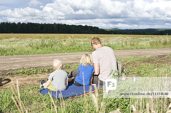 Father and sons sitting in meadow by dirt road
