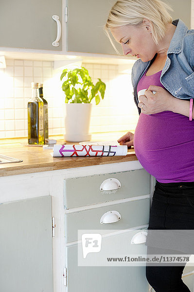 Schwangere Frau liest Zeitschrift in der Küche