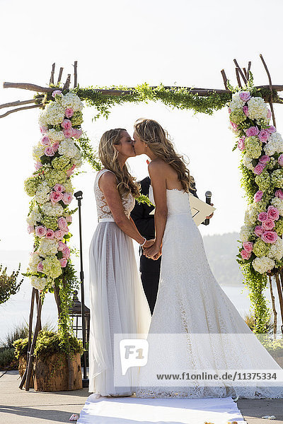 Caucasian brides kissing at wedding ceremony