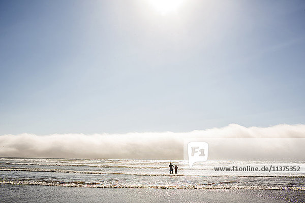 Caucasian mother and son wading in ocean waves at beach