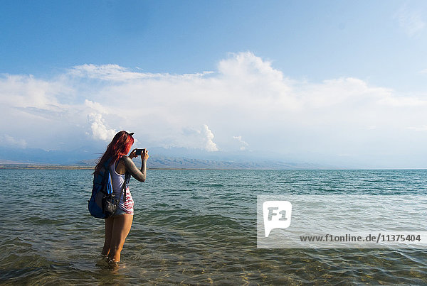 Kaukasische Frau watet im Meer und fotografiert mit dem Handy