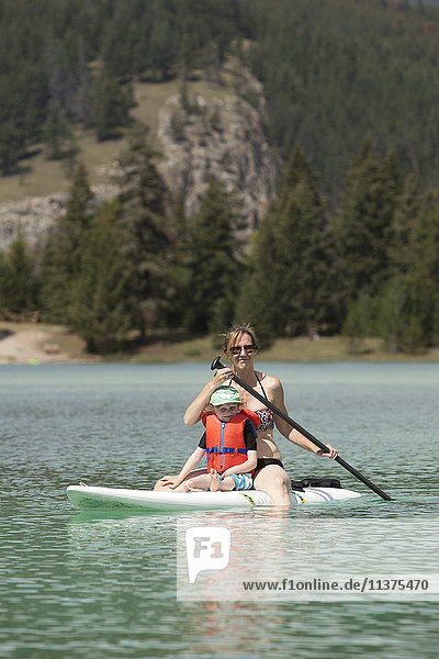Caucasian mother and son sitting on paddleboard on lake