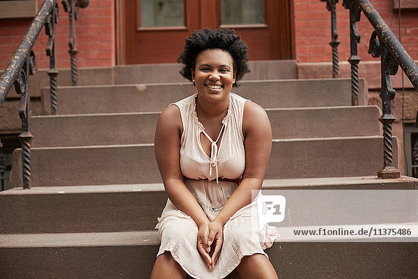 Porträt einer lächelnden schwarzen Frau  die auf einer städtischen Treppe sitzt