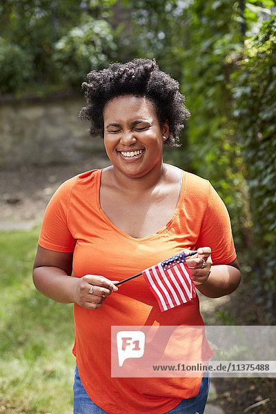 Porträt einer lachenden schwarzen Frau  die eine kleine amerikanische Flagge hält