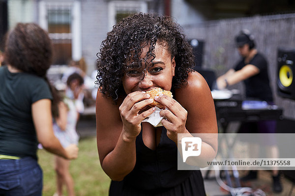 Mixed Race woman eating hamburger at backyard party