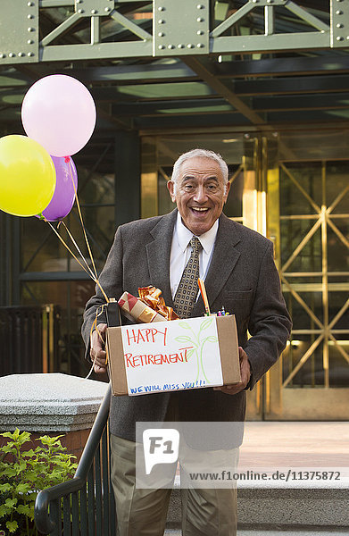 Hispanic man carrying belongings with happy retirement sign and balloons