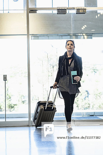Hispanische Frau mit Reisepass beim Ziehen des Koffers im Flughafen