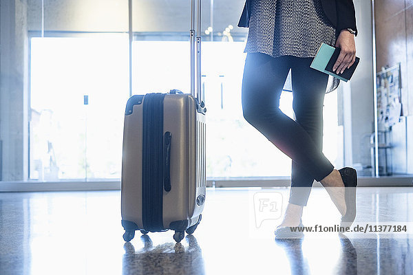 Hispanische Frau mit Reisepass und Koffer auf dem Flughafen